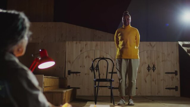 Young Black actress walking on theatre stage, sitting on chair and talking with director while passing audition
