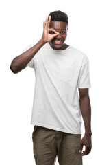 Fototapeta premium Young african american man wearing white t-shirt doing ok gesture with hand smiling, eye looking through fingers with happy face.