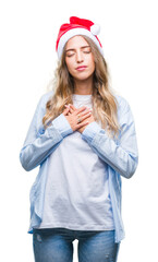 Beautiful young blonde woman wearing christmas hat over isolated background smiling with hands on chest with closed eyes and grateful gesture on face. Health concept.