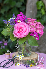romantischer Blumenstrauß mit pink Rose, Hortensienblüten, Wicken, Lavendel und Mutterkraut in Glasvase im Garten