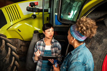 Two female farmers discussing with tablet in farm workshop