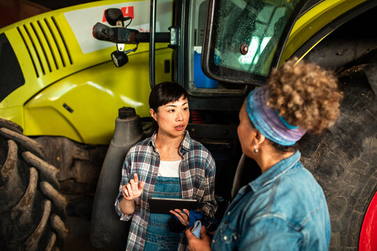 Two female farmers discussing with tablet in farm workshop