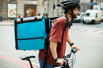 Delivery man with large backpack riding bicycle in urban setting