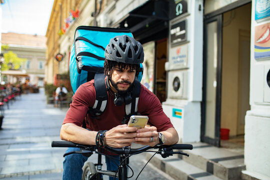 Delivery man checking smartphone while standing with bicycle on city street