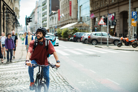 Delivery man with large backpack riding bicycle in urban setting