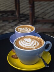 Two cups of cappuccino in colorful cups mugs blue and yellow on a low table