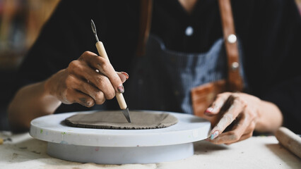 Close up of a person using a sculpting tool to shape a flat piece of clay on a pottery wheel, focused on the detailed work in a creative studio, Crafts and DIY concept