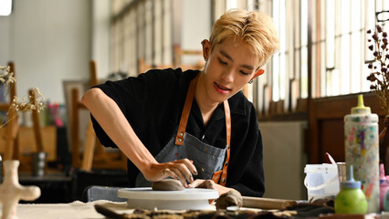 an LGBT person with braces, wearing an apron, pressing clay to form a shape on a pottery wheel....
