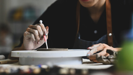 Close-up of a person wearing an apron decorating patterns on clay with a tool, focusing intently, working on a pottery wheel in a creative studio, Crafts and DIY concept