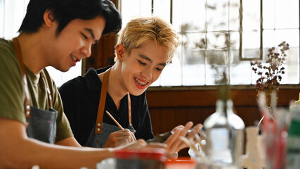 Two friends, one LGBT, are joyfully working on an art project together. Both are focused and enjoying their creative time in a sunlit room filled with art supplies, Crafts and DIY with people concept