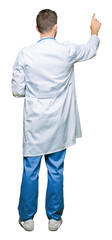 Handsome doctor man wearing medical uniform over isolated background Posing backwards pointing behind with finger hand