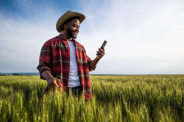Young farmer using mobile phone while standing in his growing wheat field.	