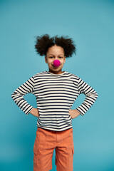 A young African American girl with curly hair poses with a playful red nose against a bright blue background.