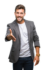Young handsome business man over isolated background smiling friendly offering handshake as greeting and welcoming. Successful business.