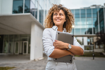 Business woman stand in front business building hold laptop