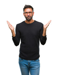 Fototapeta premium Adult hispanic man wearing glasses over isolated background clueless and confused expression with arms and hands raised. Doubt concept.