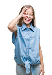 Young beautiful girl over isolated background doing ok gesture with hand smiling, eye looking through fingers with happy face.