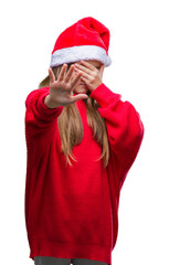 Young beautiful girl wearing christmas hat over isolated background covering eyes with hands and doing stop gesture with sad and fear expression. Embarrassed and negative concept.