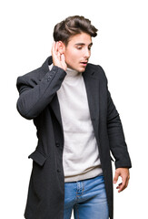 Young elegant man wearing winter coat over isolated background smiling with hand over ear listening an hearing to rumor or gossip. Deafness concept.