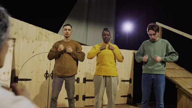 Group of young drama school students doing chest thumping exercise with female teacher during acting class in theatre