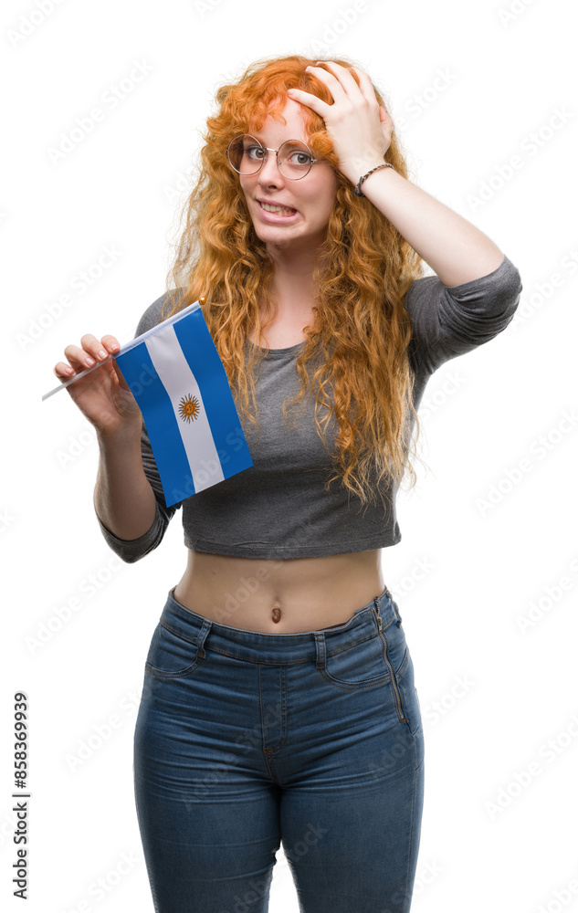 Poster young redhead woman holding flag of argentina stressed with hand on head, shocked with shame and sur