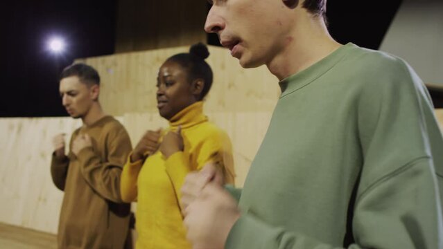 Young male actor standing on stage in theatre and thumping his chest while taking acting class in drama school