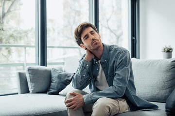 Upset tired young man feeling pain massaging stiff neck rubbing tensed muscles to relieve back ache...
