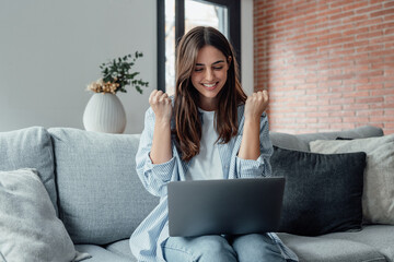 Excited emotional screams with joy woman sit on sofa hold on lap notebook makes Yes hand gesture...