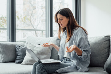 Angry young woman sit on sofa in living room frustrated having operational problems working on...