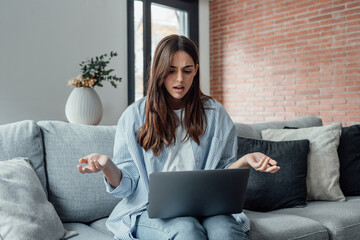 Angry young woman sit on sofa in living room frustrated having operational problems working on laptop, mad millennial girl feel stressed confused with slow internet connection or computer spam.