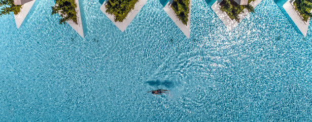 Top view of a women in swimming pool with white graphic potteries and trees 