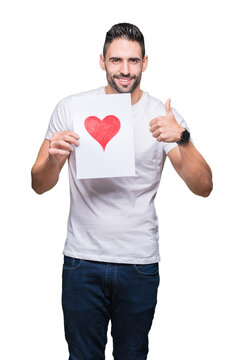 Handsome young man holding card with red heart over isolated background happy with big smile doing ok sign, thumb up with fingers, excellent sign