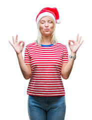 Young beautiful blonde woman wearing christmas hat over isolated background relax and smiling with eyes closed doing meditation gesture with fingers. Yoga concept.