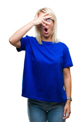 Young beautiful blonde woman wearing glasses over isolated background peeking in shock covering face and eyes with hand, looking through fingers with embarrassed expression.