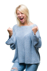 Young beautiful blonde woman wearing winter sweater over isolated background very happy and excited doing winner gesture with arms raised, smiling and screaming for success. Celebration concept.