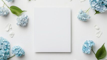 Blank white mockup frame surrounded by blue hydrangea flowers and green leaves, perfect for showcasing artwork or invitations.