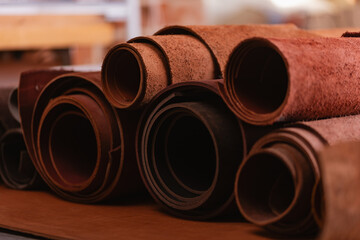 Different brown rolls of natural color leather on rack in workshop. Materials for footwear and DIY handmade craft product