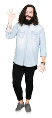 Obraz premium Young hipster man with long hair and beard wearing glasses smiling positive doing ok sign with hand and fingers. Successful expression.