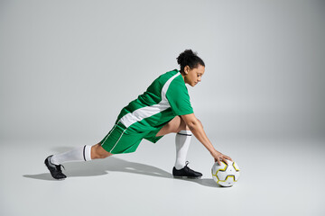 Female athlete in green jersey stretching on white studio floor, reaching for soccer ball.