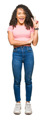 Young beautiful woman with curly hair wearing pink t-shirt smiling with happy face winking at the...