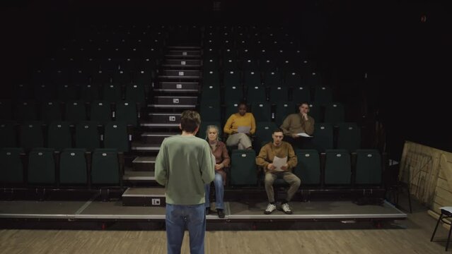 Professional actor going from stage to colleagues sitting in audience and performing his monologue in front of them during rehearsal or audition in theatre