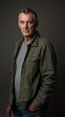 Obraz premium Middle-aged man with gray hair and beard in green jacket, stares at camera against gray background