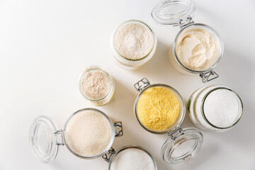 food storage, culinary and eating concept - close up of jars with different kind of flour, salt and sugar on white background, top view
