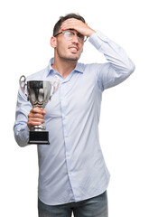 Handsome young man holding trophy stressed with hand on head, shocked with shame and surprise face, angry and frustrated. Fear and upset for mistake.