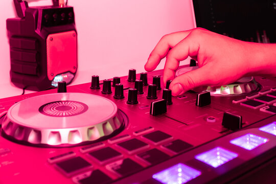 Hand manipulating a DJ controller in a vivid pink light