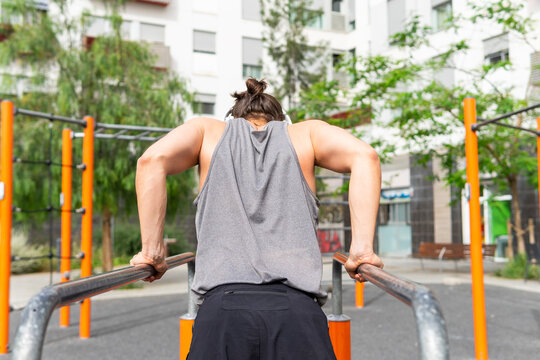 Anonymous man training on parallel bars in urban park