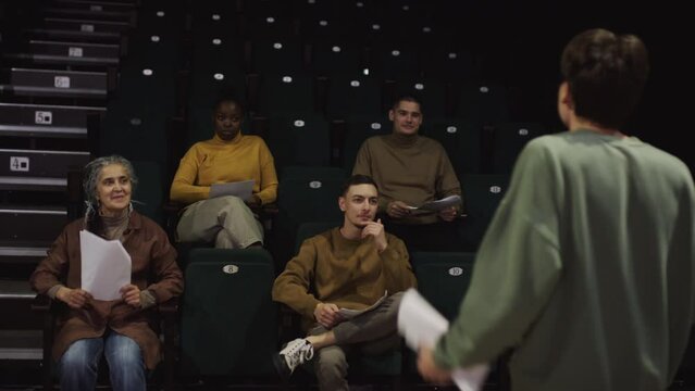 Cheerful drama teacher and group of diverse students sitting in audience and smiling while watching expressive performance of young actor on theatre stage during rehearsal