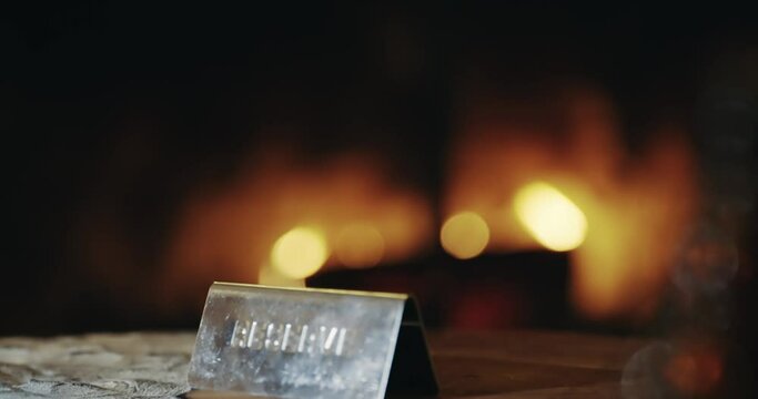 Close-up of a 'Reserve' sign on a wooden table, set against a softly lit, inviting fireplace in a luxurious hotel. Perfect for conveying exclusive, reserved settings.