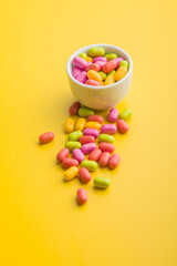 Colorful hard mint Candies in bowl on yellow background.