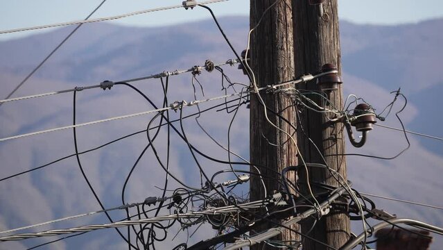 Complex network of electric wires on a wooden pole. Close-up view of a chaotic tangle of electric wires and connections on a wooden utility pole, against a mountainous backdrop.